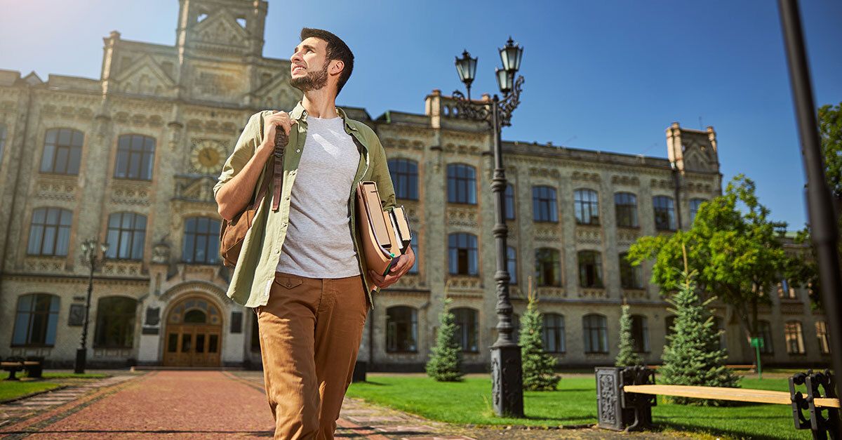Joven con mochila y libros caminando frente a una universidad en España